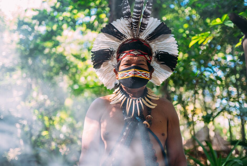 Homem indígena com cocar tradicional em uma floresta